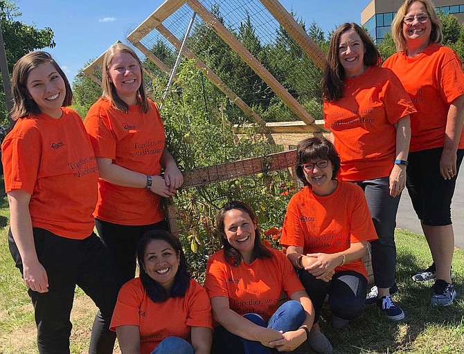 WFCM staff members in their garden that helps provide clients with fresh vegetables. Standing, from left are Grace Foust, Client Services Director; Harmonie Taddeo, Executive Director; Jennie Bush, Community Outreach Manager; and Debbie Culbertson, Food Pantry Assistant Manager/Volunteer Coordinator. Sitting, from left are Dolly Bonta-Reavis, Client Intake Assistant; Pamela Montesinos, Food Pantry Director; and Mary Ellen D'Andrea, Development Director. (Not pictured: Lillian Diaz, Client Support Specialist). Orange is the national color of hunger, and their Hunger Action Month T-shirts read, “Together we can #EndHungerHere.”