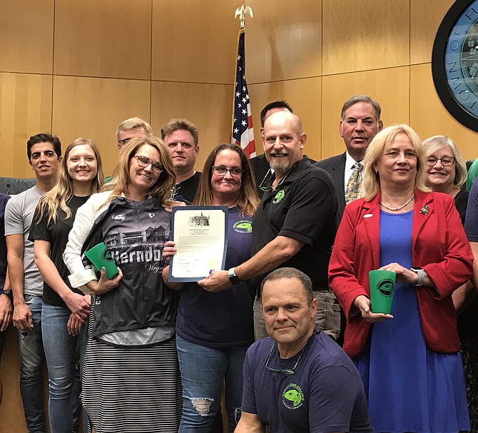 Lisa C. Merkel, Mayor of the Town of Herndon, holds a gifted commemorative Green Lizard Cycling jersey while Beth and Dave Meyer, co-owners of Green Lizard Cycling, show off the proclamation presented to them by the mayor and town council on Tuesday, Sept. 10, 2019.