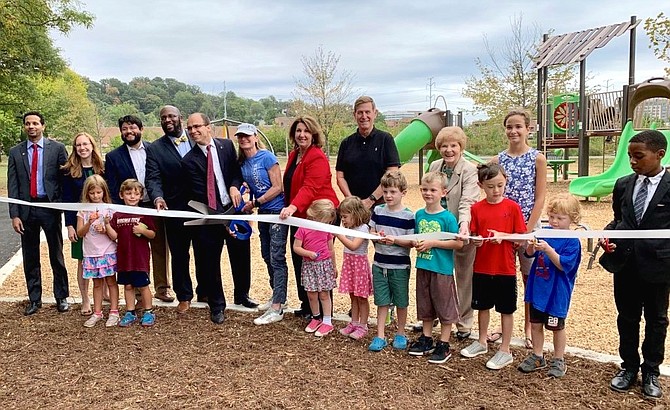 Brooke Curran, center, holding scissors, is joined by elected officials and local children at the official opening of the Four Mile Run playground Sept. 14 in Arlandria. Curran’s RunningBrook nonprofit worked with the city and local donors to build the community playground.