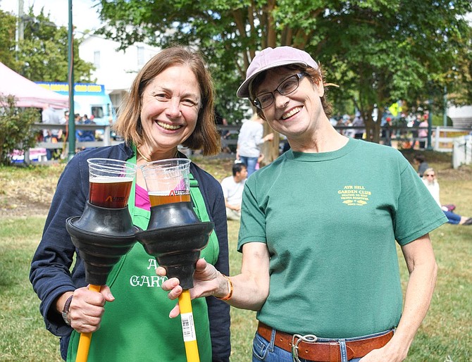 Nancy Moats and Christina Wren of Ayr Hill Garden Club use their free plungers given out by My Plumber as beer holders.