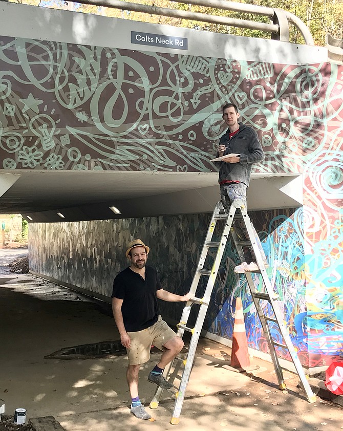 Artist Ben Volta talks with James Tafel Shuster as he paints panel edges to ensure color consistency of the massive Colts Neck Road Underpass mural in Reston.