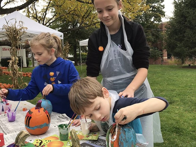 Addysen Moore-Brewer, 9, of Centreville joins her brother, Landon, 5, while older sister, Jamie, 12, keeps things in check at the pumpkin painting table, part of Pumpkin Palooza on the Herndon Town Hall Square. The children's mother Stephanie works at Herndon Parks and Recreation.