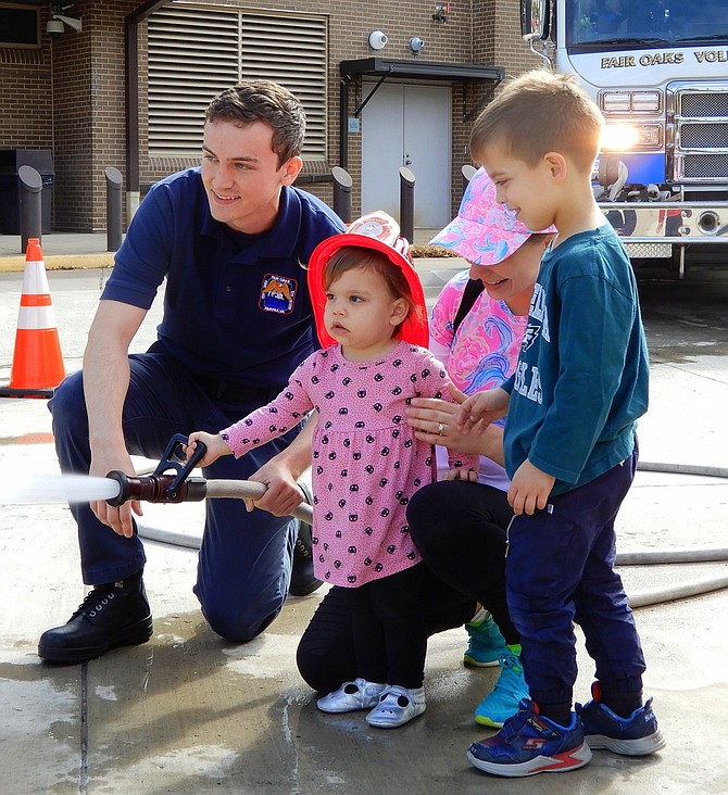 Recruit firefighter Matt Brunini helps Lilly Strickler, 1½, squirt water from a fire hose while her mom, Marisa, and brother Gordie, 4, watch.
