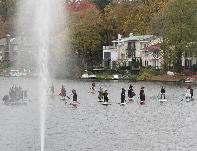A playful coven of Halloween witches on stand up paddle boards (SUPs) skim the waters of Lake Anne in Reston to kick off an evening of play and spooky brews.