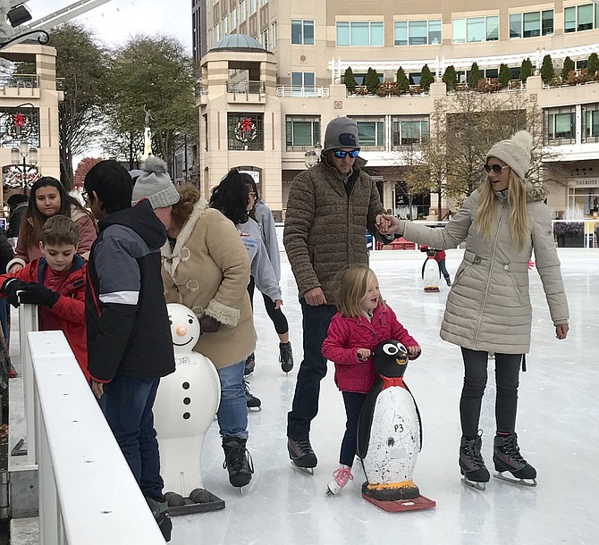 Cole Hilling, Savannah Myzk and Denver, 5, have the outdoor ice-skating requirements down pat: puffy coats, penguin skate-aid, a little hand-holding and smiles during the 2019 opening weekend for Reston Town Center public ice-skating at the Pavilion.