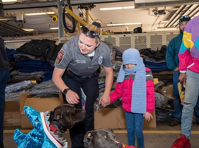 Holding the hand of a Fairfax County Police officer, a Gum Springs preschooler visits with the Caring Angels therapy dogs at the Fairfax County Firefighters coat drive distribution Oct. 28 at Fire Station 11.