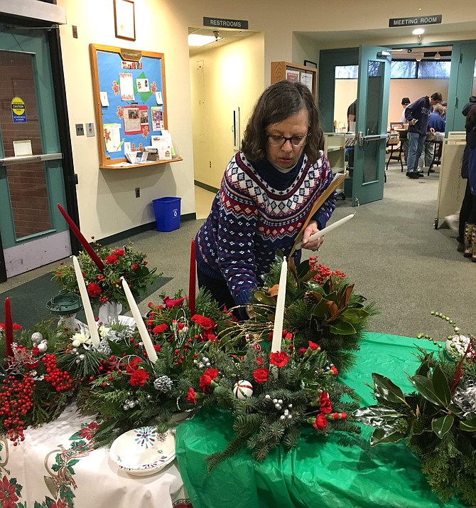 Carol Dietzel adds candles to arrangements at the annual Potomac Village Garden Club Holiday Greens Arrangements sale Saturday.