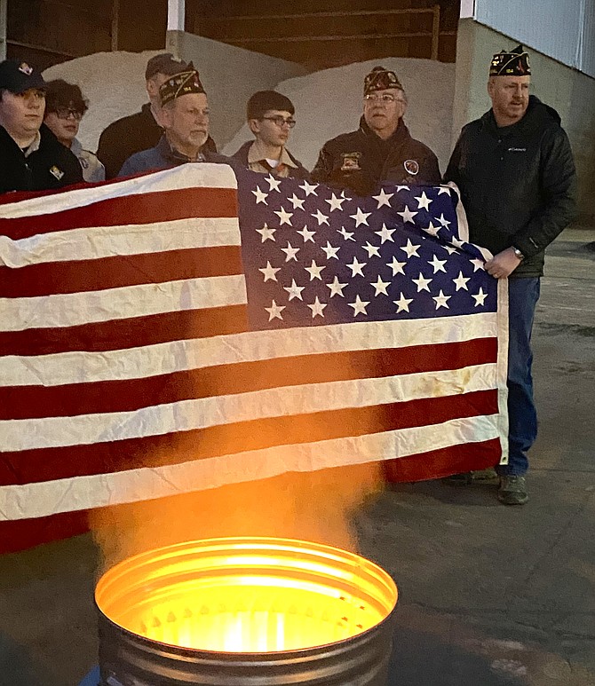 Members of The Wayne M. Kidwell American Legion Post 184 Herndon-Reston and Scouts of Troop 1570 of the National Capital Area Council, Powhatan District in Herndon, unwrap an unserviceable and worn casket flag, preparing it for retirement by burning.