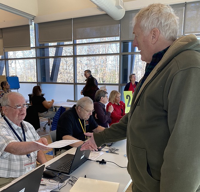 On Feb. 22, 2020, Charlie Quinn, a Fairfax County Elections Officer at the North County Absentee Satellite office in Reston, hands a paper to Rob Loesch of Reston, an in-person absentee voter.