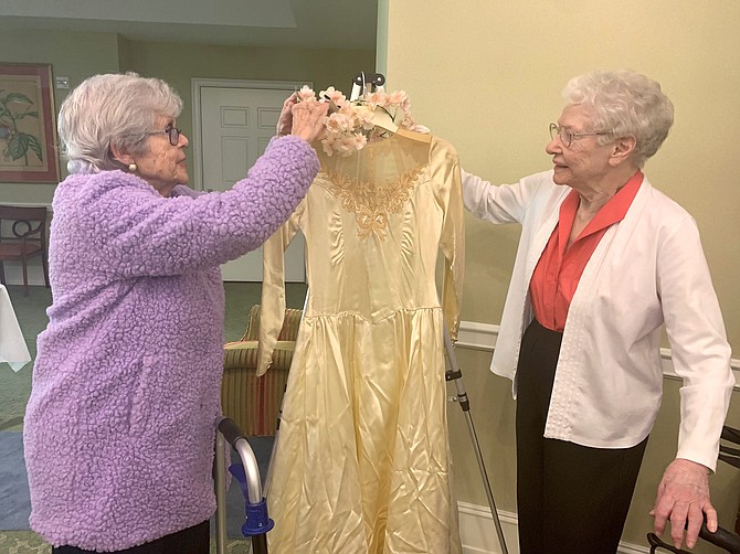 Nancy Gamble and Betsy Ramirez of Goodwin House Alexandria adjust the neckline of the 1940s wedding dress featured at the Feb. 14 Lasting Love Wedding Expo display of wedding gowns and photographs.