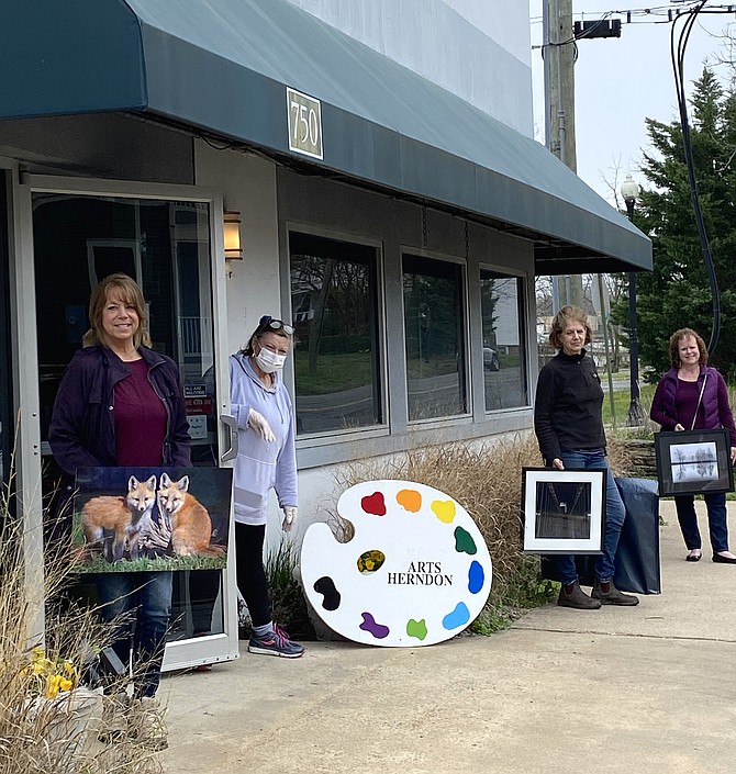 Finalists in the 11th Annual Photography Exhibit pick up their works after Arts Herndon cancels the Exhibit and Reception due to COVID-19. From left on sidewalk: Photographers Suzanne Stout of Potomac Falls, Sarah Strickler of Arlington and Janet Sifers of Oak Hill. Masked, President & CEO of Arts Herndon, Jo Ormesher, holds the door open.