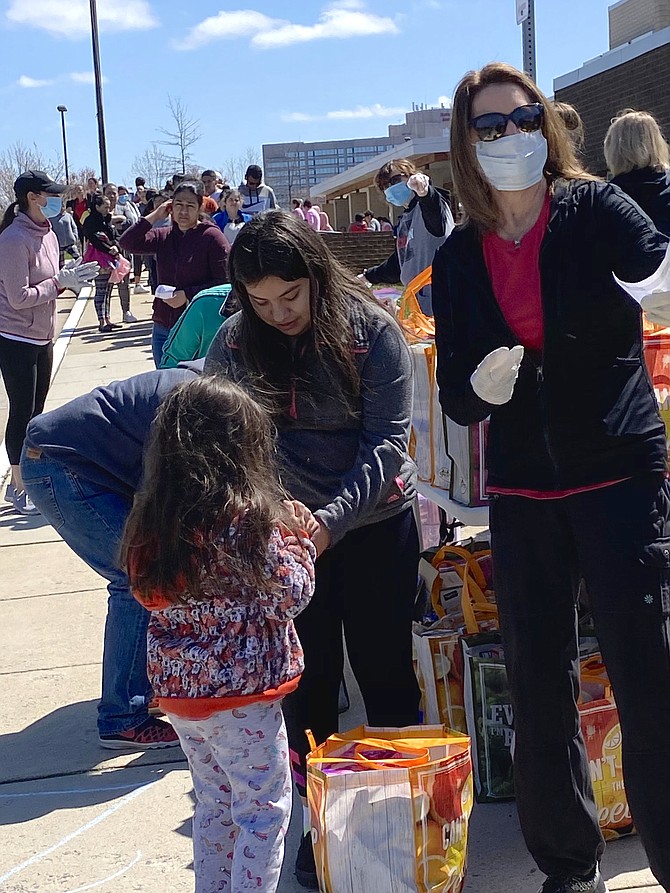 In Herndon, patrons in need of food line up in family groups, socially distant from other families, to receive bagged items from masked and gloved Food for Neighbors volunteers as the number of confirmed coronavirus cases mounts.