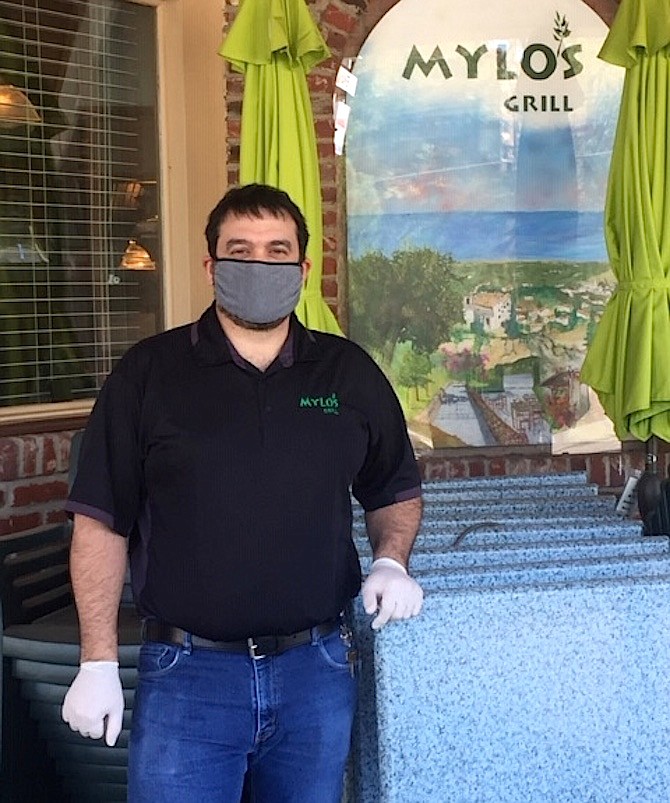 Curbside service has replaced restaurant dining as Chris Mylonas stands outside Mylo’s Grill with patio tables piled high.