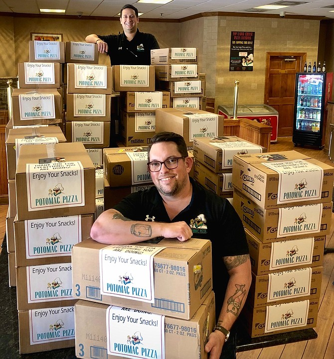 Chris Martin, community relations manager for Potomac Pizza, and Andy Goldstein, senior manager, stand by boxes of snacks to be donated by Potomac Pizza to workers at area hospitals.