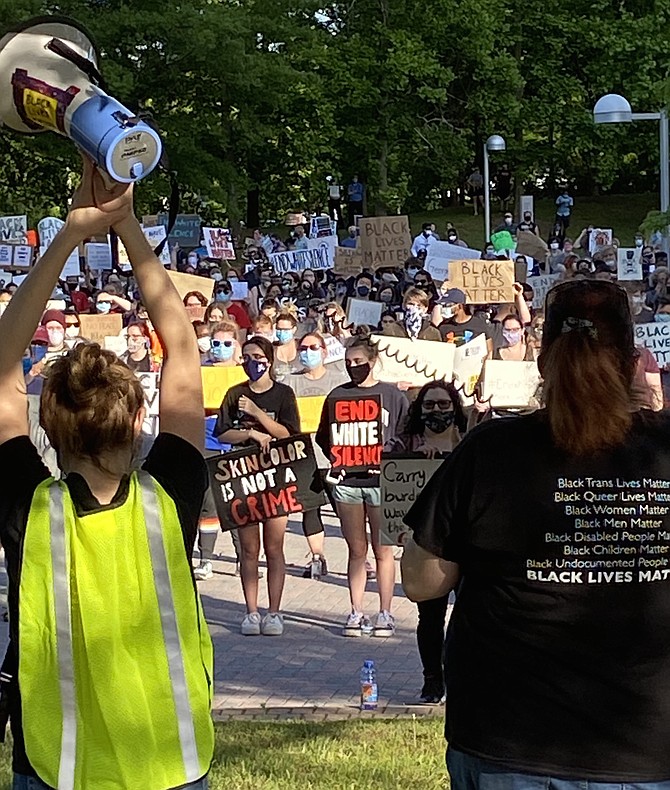 (Right) Cayce Utley, a member of SURJ NoVa chants into the speaker, "White silence is violence," while a volunteer holds up the megaphone bullhorn.