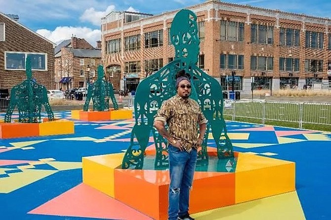 Artist Olalekan Jeyifous standing with Wrought, Knit, Labors, Legacies, a new public art exhibit at the Alexandria waterfront.