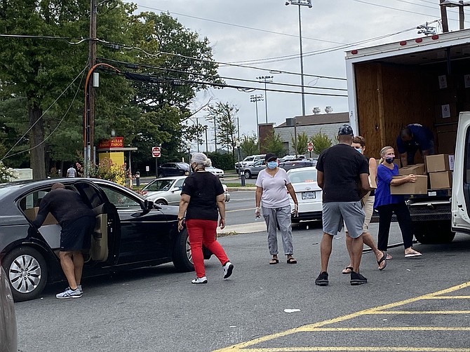 People in cars, on foot, and even on bicycles arrive to receive free boxes of food at the 7-Eleven in the Town of Herndon distributed by volunteers and members of  Heritage Fellowship Church.