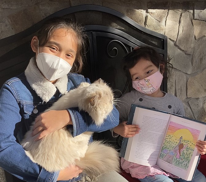 Petra Demas, 10, of Great Falls holds Mima the family cat, as her little sister, Briella, 3, shows the kitty Petra's winning illustration featured in J.K. Rowling's book, "The Ickabog."