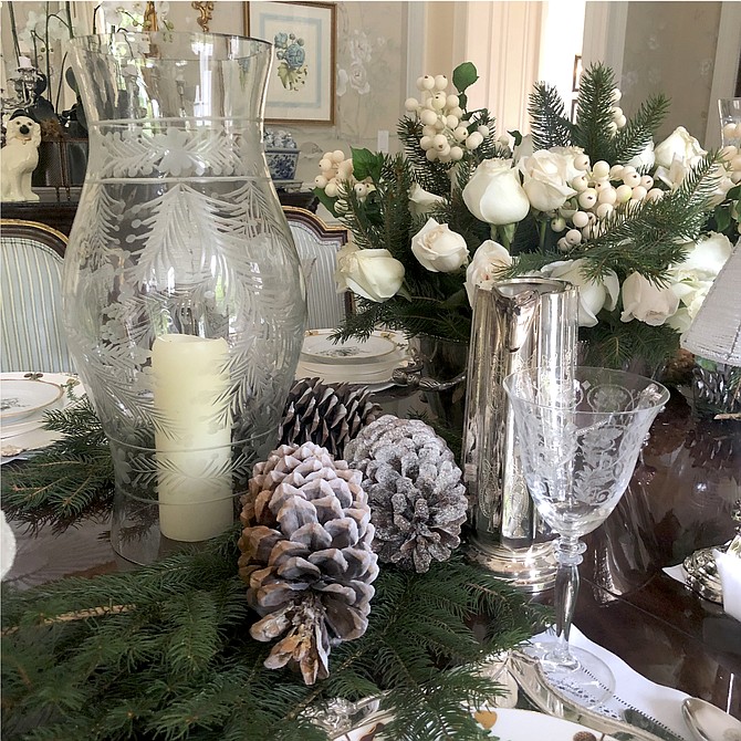 Etched hurricanes mixed with greenery and pine cones create an elegant tablescape.