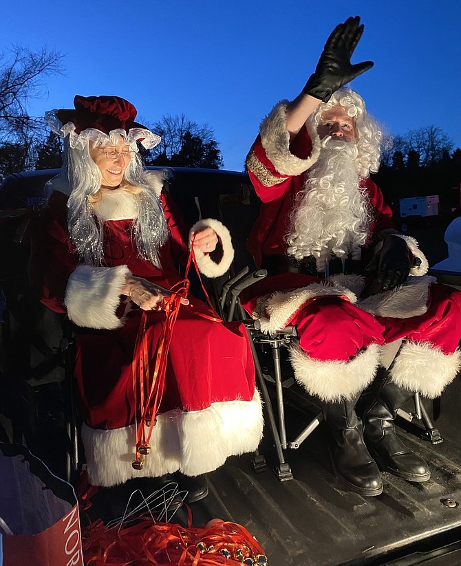 Santa waves from the back of the truck while Mrs. Claus untangles the bell necklaces for the elves to distribute to children in this year’s Christmas Tree Lighting in Great Falls.