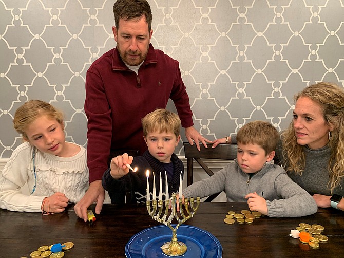 Ollie Friedberg, 6,  lights the first candle of a Hanukkah with the Shamash, the attendant candle used to light the other candles, as part of the fifth night of Hanukkah observance on Dec. 14. With Ollie are sister Madi, 9, twin brother Noah and parents Christine and Michael.