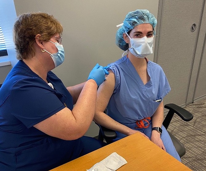 Christine Knoell, RN (left), vaccinates Dr. Kathleen Sachse (right) during the first days of the Reston Hospital Center Pfizer-BioNTech COVID-19 Vaccine effort for healthcare providers.
