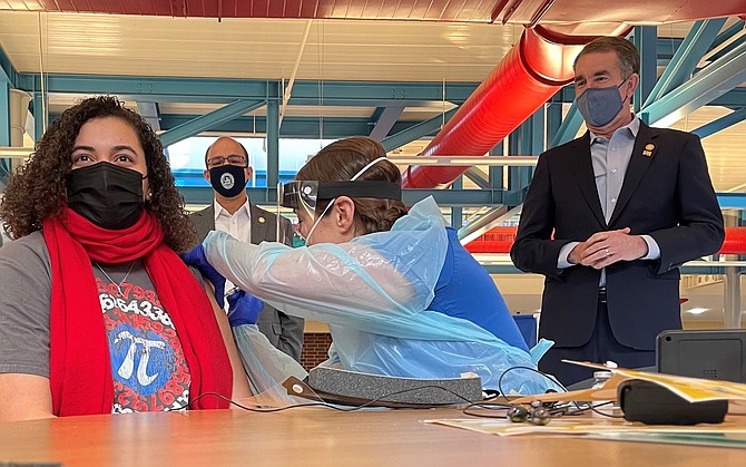 T.C. Williams High School geometry teacher Danielle Thorne, left, receives a COVID-19 vaccine from nurse Leanne Desmond Jan. 12 as Mayor Justin Wilson and Gov. Ralph Northam look on. The Alexandria event kicked off the Phase 1B vaccinations for ACPS employees.