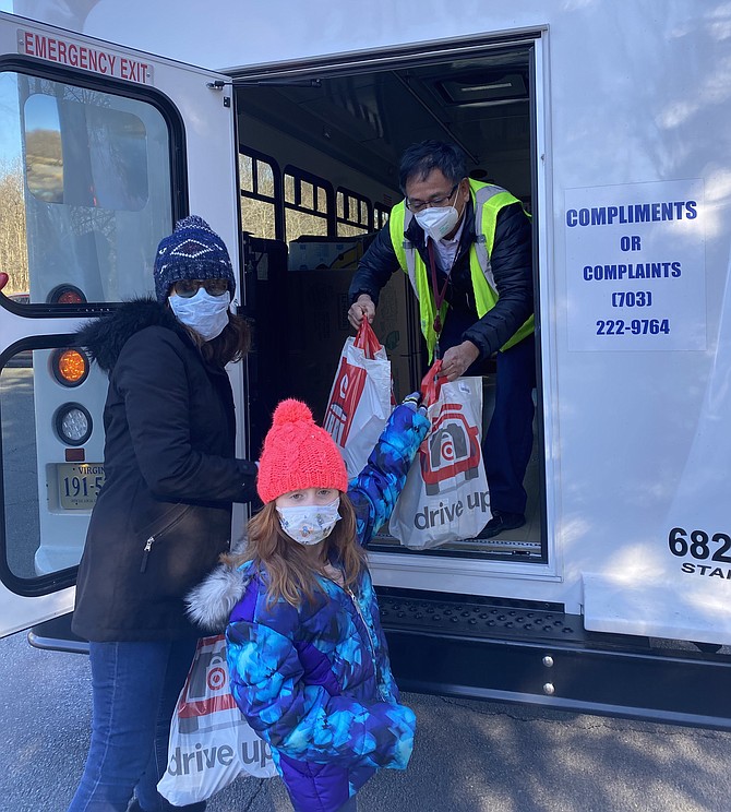 Hannah Morgan, 7, hands her food donation bag to Manuel Cavero, a Fairfax County MV Transportation Fastran Bus Driver, to place on the bus located at the Great Falls Library parking lot during the Jan. 30 Stuff the Bus food drive.