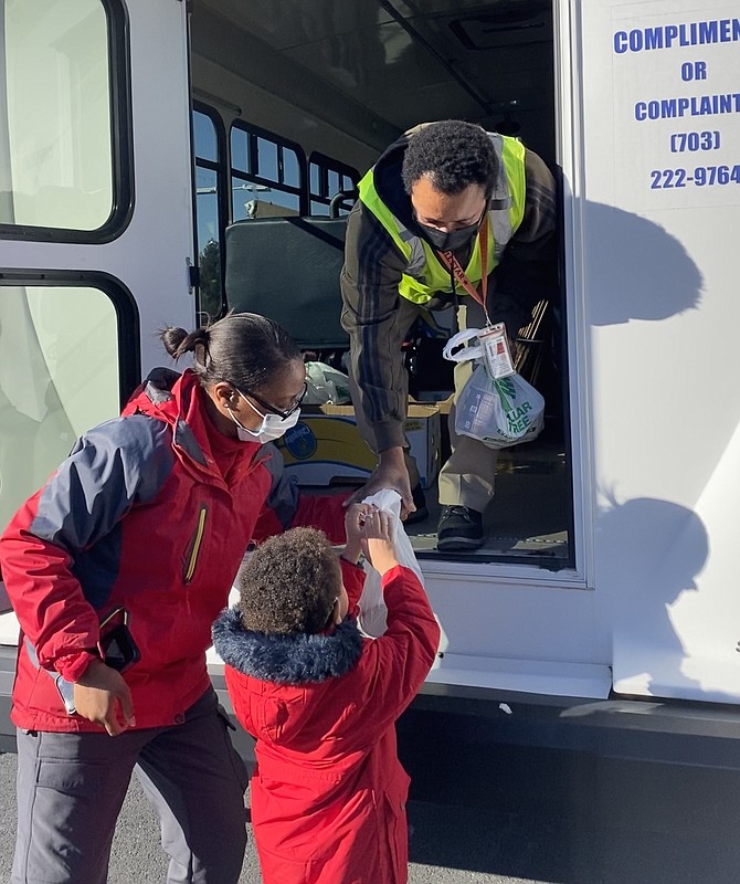 With a little help from his mother, Esther Fausett,  Solomon, 5, of Reston hands his food donation bag to Jose Gomes, Fairfax County MV Transportation Fastran Bus Driver in the parking lot of the Hunter Mill District Supervisor's Office, one of the 21 Countywide Stuff the Bus donation locations on Jan. 30.