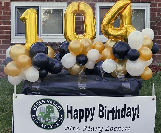 Mary Lockett’s house and yard are festooned with balloons and signs to celebrate her 104th birthday as neighbors dance across the street.