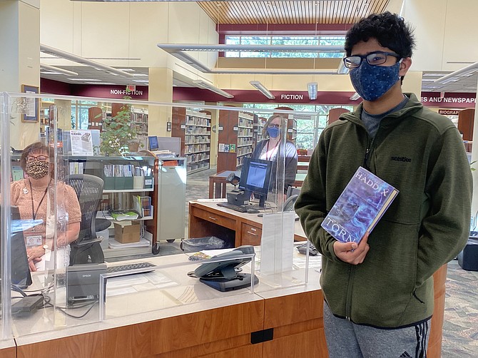 Arnav Ketineni, 13, of Great Falls and a student at Cooper Middle School in McLean, prepares to check out “The Missing: Torn, Book Four” by Margaret Peterson Haddix, with the help of Sandy Souleles, Information Assistant, Fairfax County Library. Rebecca Wolff, Librarian II Fairfax County, stands to the side.