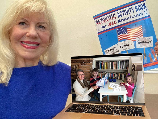 Reston author Audrey Adair holds up her newest release, Patriotic Activity Book for ALL Americans. On the screen is a live shot of her two grandchildren and daughter, Allison Albert, completing a book project.