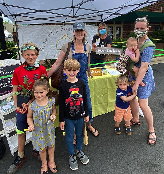 (From left) The Moriarty and DeHaan families of Herndon enjoy a morning at the Herndon Farmers Market, stopping by the vendor booth of Bees of a Feather Farm, located in Great Falls, owned and operated by Carrie Clark.