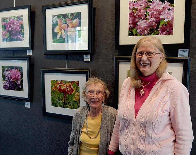 Maxine Turner and Dee Leggett in front of the display of Maxine’s flower photographs at TD Bank in Great Falls.