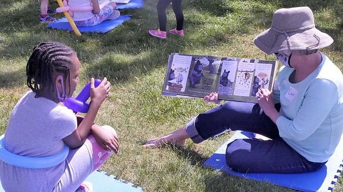 Carol Dawson sits on a lawn pad reading a Mother Bruce book at the Parade of Animals book event. She has chosen her animal-themed stories to fit today’s theme.