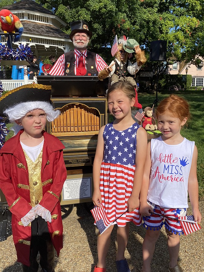 John Maloney, 5, of Great Falls, joins Ella DeTrani, 6, of McLean and her sister, Lia, 5, after listening to Terry Bender of Great Falls explain how the organ grinder plays music.