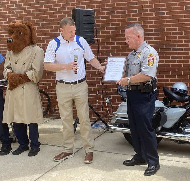 With McGruff the Crime Dog facing forward, Jeffrey C. McKay, Chairman of the Fairfax County Board of Supervisors, hands Kevin Davis, Chief of Police Fairfax County, the Proclamation by the Board of Supervisors on behalf of all residents of Fairfax County proclaiming Tuesday, Aug. 3, National Night Out.