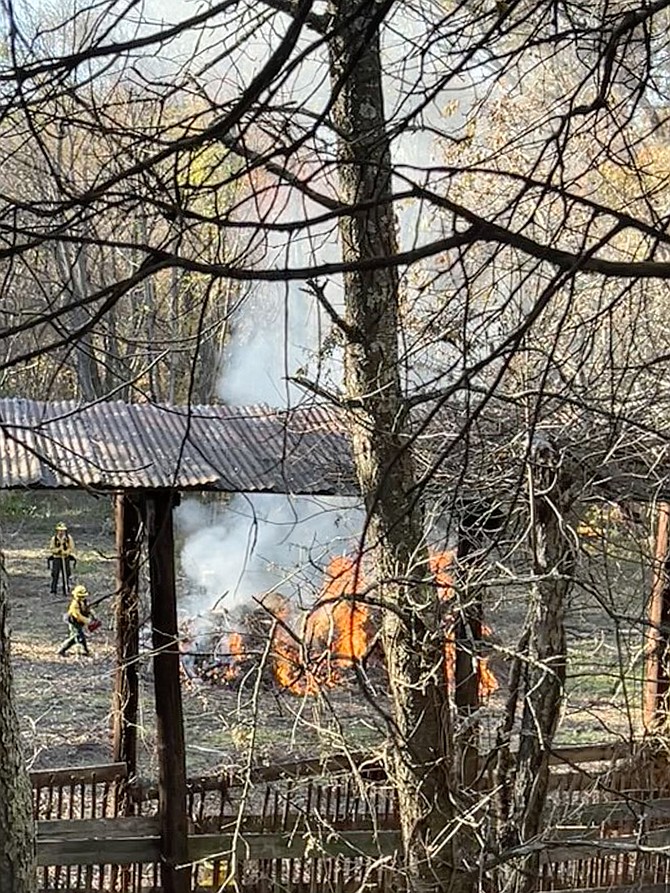 In another section of the reforestation area a large debris pile is ignited after water is sprayed on the historic corn crib and surrounding ground to protect the structure.