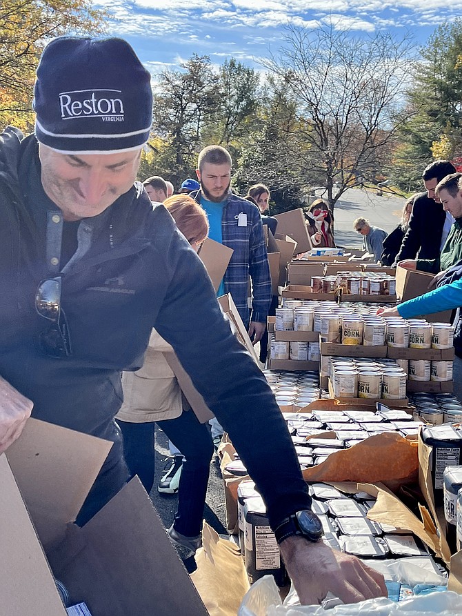 Scott Plank, CEO of War Horse Cities, one of Reston National Golf Course owners, walks down the Thanksgiving Day Food assembly line, carefully packing items for Cornerstones, but his box rips apart unexpectedly. Plank accepts the challenge with a smile, retrieves the items, and repacks a new box.
