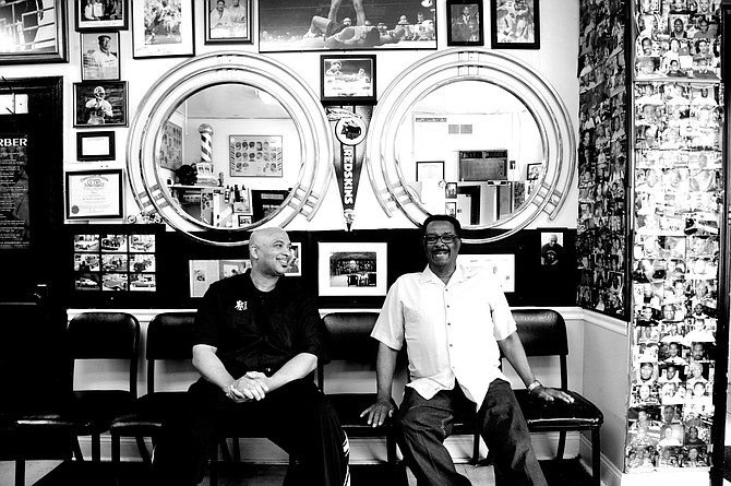 Father and son at Moore’s Barber Shop in Arlington, with photos of clients and other memorabilia on the wall.