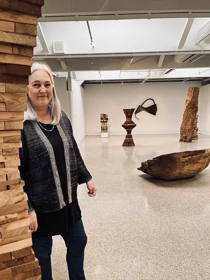 Nancy Sausser, curator of the McLean Project for Arts, stands among contemporary wood sculpture by four artists: Emilie Beneš Brzezinski, Rachel Rotenberg, Foon Sham, and Norma Schwartz, at the exhibition "Give and Take: Building Form" in the McLean Community Center's Emerson Gallery.
