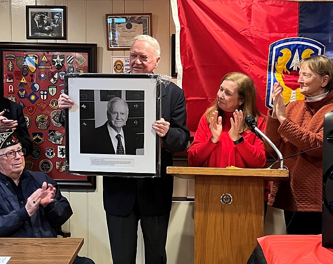 U.S. Navy Capt. Eugene “Red” McDaniel (ret.) holds the Living Legends of Alexandria portrait presented to him March 26 at American Legion Post 24 in recognition of National Vietnam War Veterans Day. Presenting the portrait to McDaniel, a POW for six years in Vietnam, were, at right, LLA board officers Gayle Reuter and Pat Miller.