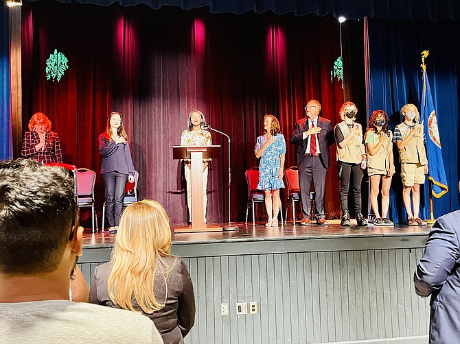 Third from left, vocalist Jordyn Jones of the Vienna Youth Players sings the national anthem as (far left to right) Kimberly Zanotti, Washington Field Office Director, USCIS; Avril Haines, Director of National Intelligence; Linda J. Colbert, mayor of the Town of Vienna; Max Carroll, supervisory Immigration services officer, USIC; and members of Girl Scout Troops 50157 and 1489 stand and place their hands over their hearts.