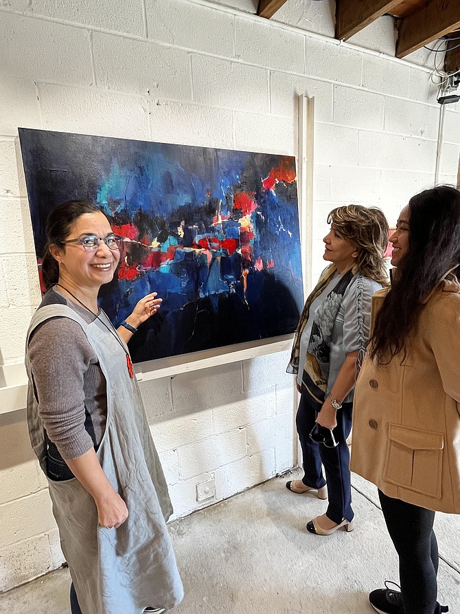 A rtist Parinaz Ziai Bahadori displays her acrylic on canvas work "Too Darn Hot" in her home studio, a renovated barn. Paranaz donates ten percent of the purchase price to refugees. She is joined by Guiti Shahabadi of McLean and Mae Villacortes of Fairfax.