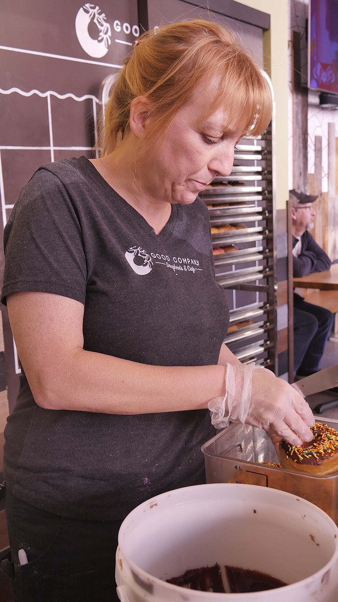 Kate Murphy, one of the owners of Good Company Donuts, decorates chocolate frosted donuts with sprinkles.