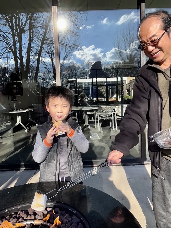 Ryan Duan, 5, of McLean, bites into his gooey s’more, loving the toasted marshmallow and layer of chocolate sandwiched between two pieces of graham cracker while his dad roasts another marshmallow.