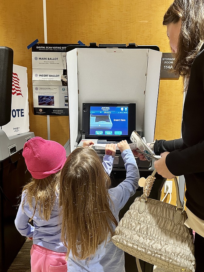 Having marked her paper ballot, voter Judee Ann Williams of Vienna helps her four-year-old twin daughters, Vivian (left) and Georgia place her ballot in the optical scan machine. The machine electronically scans the ballot, records the vote, and informs the voter that the ballot has been cast.