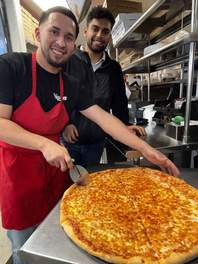 Anthony Basilios watches as Henry Amaga cuts generous slices of pizza at Deli Italiano.