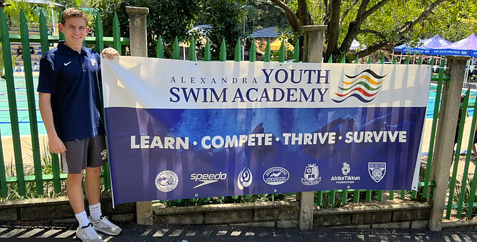 Sasha Minsky stands beside the banner for the Alexandra Youth Swim Academy.