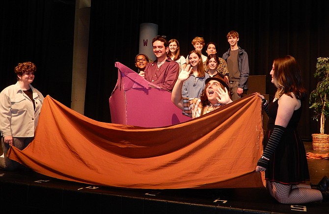 Augustus Gloop (Gabe Amiryar) falls from a boat into the chocolate river at Willy Wonka’s chocolate factory, as Wonka (Alexander Cox) smiles at the helm.